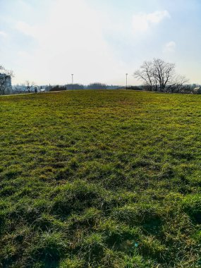 Küçük tepede çimlerle dolu büyük yeşil bir tarla. Etrafı patika ve banklarla dolu.