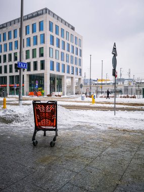 Wroclaw, Polonya - Şubat 2021: Bulutlu kış gününde alışveriş merkezinin yanındaki kaldırımda duran kırmızı alışveriş arabası