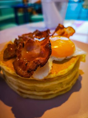 Bir yığın krep, kızarmış yumurta dilimleri, kızarmış domuz pastırması ve biraz akçaağaç şurubu.