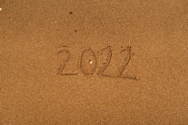 2022 está dibujando en la arena en una playa con una ola junto al mar. Vacaciones en el mar. Concepto de Año Nuevo — Foto de Stock