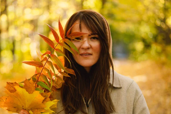 Frau im langen Hemd mit einem Strauß Herbstblätter in der Hand geht durch den herbstlichen Wald. — Stockfoto