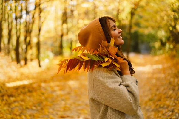 Frau im langen Hemd mit einem Strauß Herbstblätter in der Hand geht durch den herbstlichen Wald. — Stockfoto