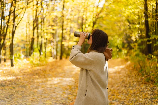 Eine junge Frau im langen Hemd mit einem Thermobecher in der Hand geht durch den herbstlichen Wald. — Stockfoto