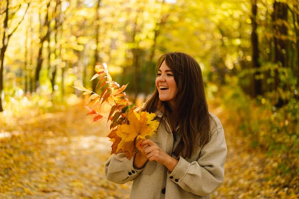 Frau im langen Hemd mit einem Strauß Herbstblätter in der Hand geht durch den herbstlichen Wald. — Stockfoto