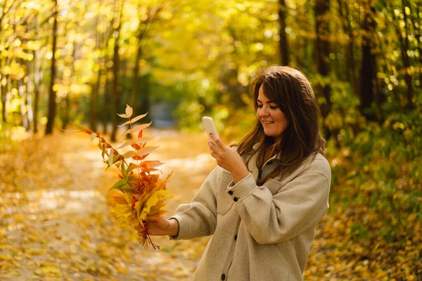 Woman in a long shirt take a photo leaves on the phone in the autumn forest. Natural landscape — Stock Photo, Image