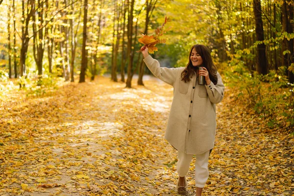 Eine junge Frau im langen Hemd mit einem Thermobecher in der Hand geht durch den herbstlichen Wald. — Stockfoto