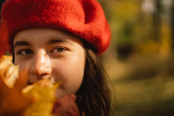 A Teengirl in a red beret with a bouquet of autumn leaves in her hands walks through the forest — Stock Photo, Image