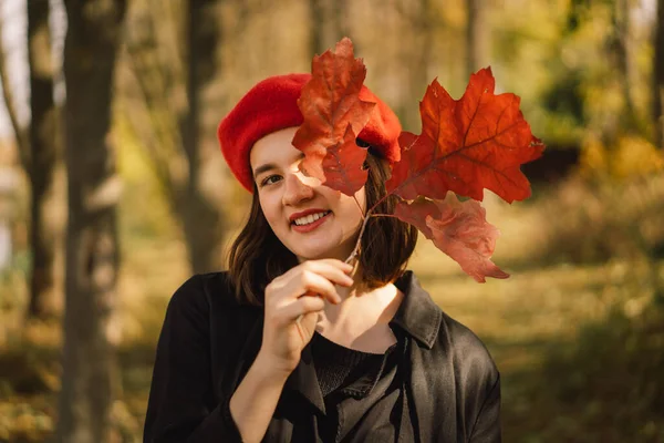 Ein Teengirl mit roter Baskenmütze und einem Strauß Herbstblätter in der Hand geht durch den Wald — Stockfoto