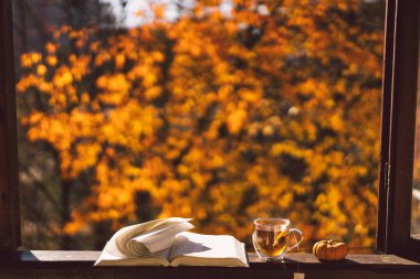 Bir fincan sıcak çay ve eski bir pencere eşiğinde açık bir kitap. Evdeki bir penceredeki natürmort hayat detayları