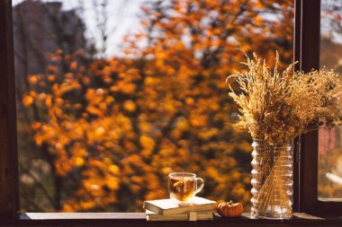 Bir fincan sıcak çay ve eski bir pencere eşiğinde açık bir kitap. Evdeki bir penceredeki natürmort hayat detayları