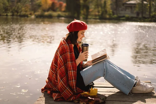 A Teengirl in a red boet reading book on wooden pontoon. Temporada de otoño. —  Fotos de Stock