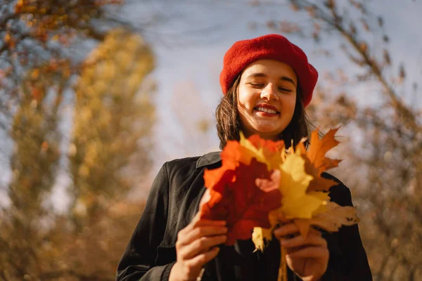 A Teengirl in a red beret with a bouquet of autumn leaves in her hands walks through the forest — Stock Photo, Image