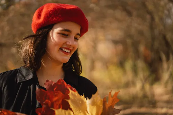 Ein Teengirl mit roter Baskenmütze und einem Strauß Herbstblätter in der Hand geht durch den Wald — Stockfoto