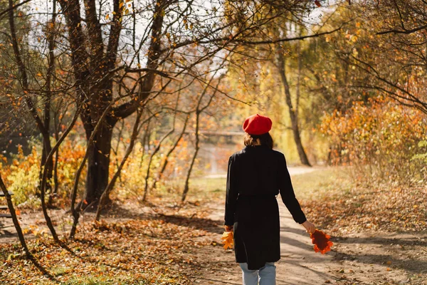 Une adolescente dans un béret rouge avec un bouquet de feuilles d'automne dans ses mains se promène dans la forêt — Photo
