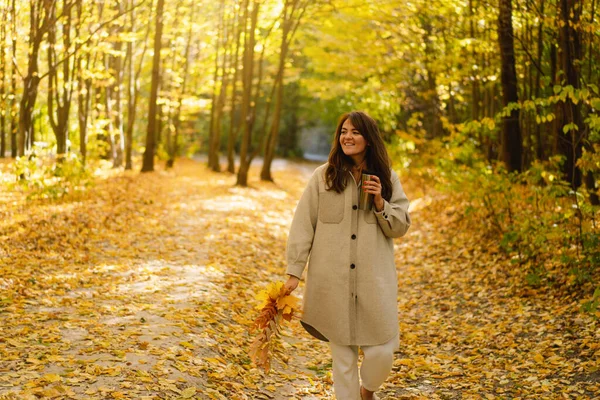 Eine junge Frau im langen Hemd mit einem Thermobecher in der Hand geht durch den herbstlichen Wald. — Stockfoto