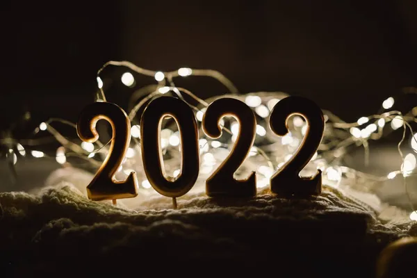 สุขสันต์วันปีใหม่ 2022. หมายเลข 2022 ทําโดยเทียนบนพื้นหลัง bokeh เทศกาลส่องแสงในความมืด — ภาพถ่ายสต็อก