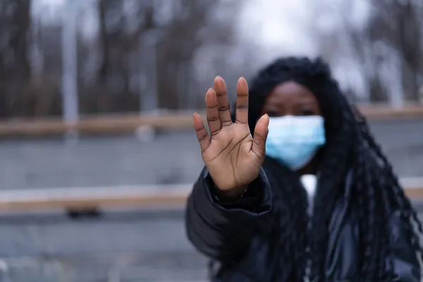 Afro lány arcorvosi maszkkal a szabadban. A fiatal afro lány kézzel jelenik meg, hogy megállítsa a koronavírust. — Stock Fotó