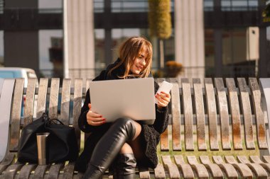Şehirdeki bir bankta oturan bir kadın bilgisayar ve telefon kullanıyor. Serbest kadın..