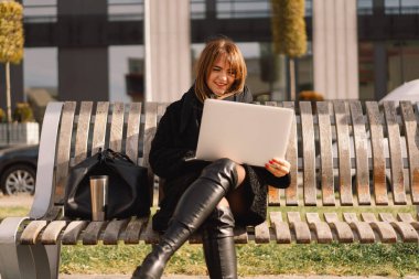 Şehirdeki bir bankta oturan bir kadın bilgisayar kullanıyor. Serbest kadın..