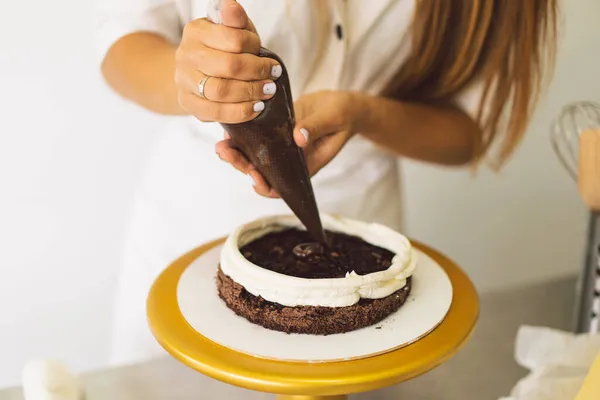 菓子の女の子は白いクリームとチョコレートでケーキビスケットを準備しています。ケーキを作る. — ストック写真