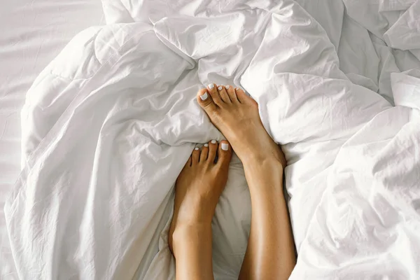 Kaki wanita dengan pedikur putih di tempat tidur putih di kamar tidur. Perawatan kaki, pedikur. Perawatan tubuh spa — Stok Foto