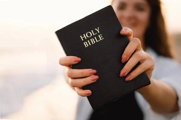 La donna cristiana tiene la Bibbia tra le mani. Leggere la Sacra Bibbia sul mare durante il bel tramonto — Foto Stock
