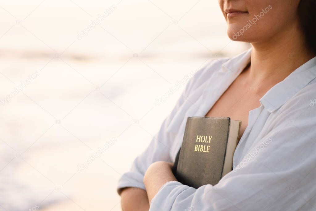 Christian woman holds bible in her hands. Reading the Holy Bible on the sea during beautiful sunset