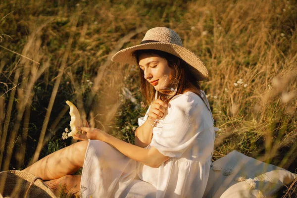Joven chica hermosa en un vestido blanco teniendo un picnic con una copa de champán o vino blanco — Foto de Stock