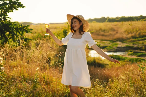 Beyaz elbiseli genç bir kız bir bardak şampanya ya da beyaz şarapla piknik yapıyor.