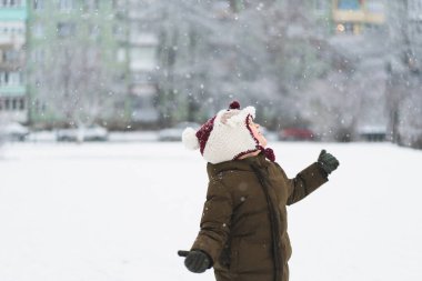 Kar yağışı sırasında komik şapkalı şirin bir çocuk yürüyor. Çocuklar için açık hava kış aktiviteleri.