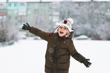 Kar yağışı sırasında komik şapkalı şirin bir çocuk yürüyor. Çocuklar için açık hava kış aktiviteleri.