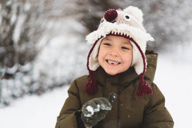 Kar yağışı sırasında komik şapkalı şirin bir çocuk yürüyor. Çocuklar için açık hava kış aktiviteleri.