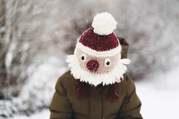 Cute little boy in funny winter hat walks during a snowfall. Outdoors winter activities for kids. — Stock Photo, Image