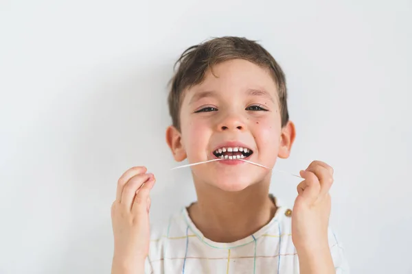 Cute boy pulling loose tooth using a dental floss. Process of removing a baby tooth.