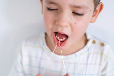 Tatlı çocuk diş ipi kullanarak dişini döküyor. Bir bebek dişini çıkarma süreci.