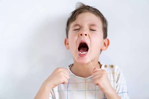 Симпатичный мальчик, вырывающий зуб зубной нитью. Процесс удаления молочного зуба. — стоковое фото