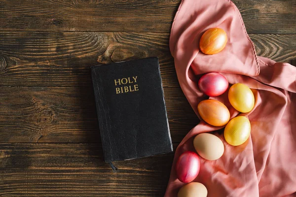 ไข่อีสเตอร์หลายสีและพระคัมภีร์ศักดิ์สิทธิ์บนพื้นหลังไม้ แนวคิดทางศาสนา — ภาพถ่ายสต็อก