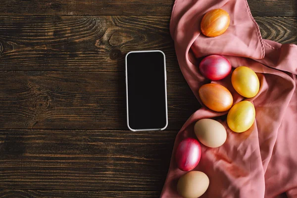 Teléfono y elegantes huevos de Pascua de color plana ponen en la mesa rústica. Espacio para texto — Foto de Stock