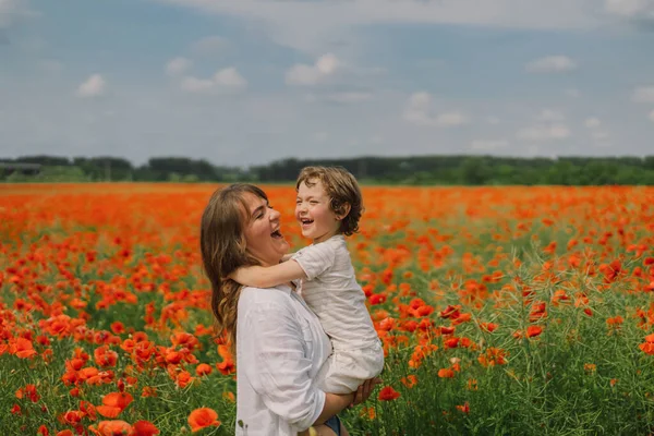 Fijne Moederdag. Kleine jongen en moeder speelt in een prachtig veld van rode klaprozen — Stockfoto