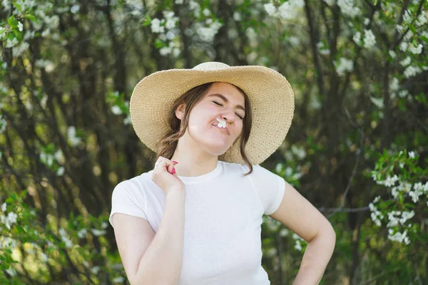 Fiatal, vicces, gyönyörű nő kalapban a virágzó fák között. Lélegezz mélyeket. Boldog nő nincs allergia — Stock Fotó