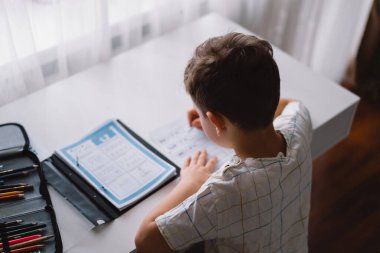 Sevimli çocuk evde ders çalışıyor ve okul ödevi yapıyor. Düşünen çocuk masada oturuyor..