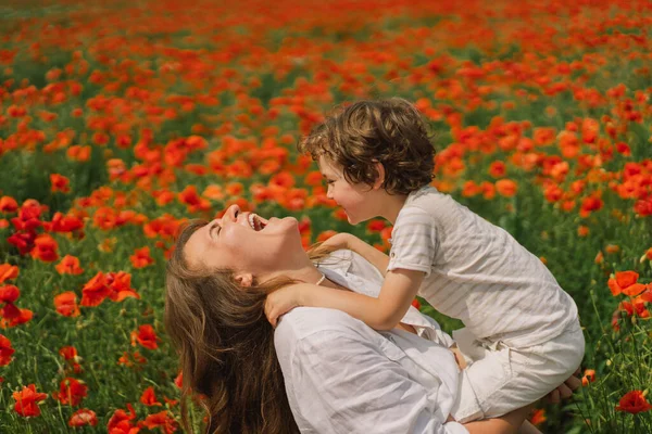 Fijne Moederdag. Kleine jongen en moeder speelt in een prachtig veld van rode klaprozen — Stockfoto