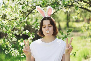 Tavşan kulaklı komik genç kız güneşli bahar bahçesinde Paskalya yumurtası avında.