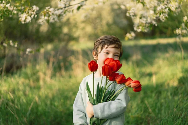 Веселый счастливый ребенок с цветочным букетом тюльпанов в природе. — стоковое фото