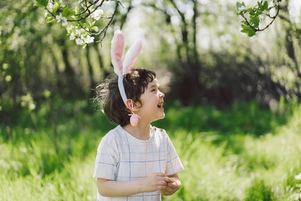 Αστείο αγόρι με αυγά καλάθι και αυτιά λαγουδάκι για το κυνήγι αυγών Πάσχα στον ηλιόλουστο κήπο άνοιξη — Φωτογραφία Αρχείου