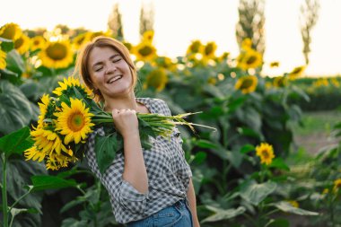 Ayçiçekli güzel bir kadın doğanın tadını çıkarıyor ve yaz ayçiçeği tarlasında gülüyor.