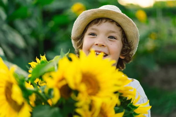 Gelukkige jongen wandelend in het veld van zonnebloemen. Kind spelen met grote bloem en plezier hebben. Stockafbeelding