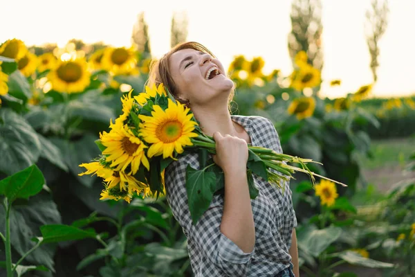 Красива молода жінка з соняшниками насолоджується природою і сміється на літньому соняшниковому полі . — стокове фото
