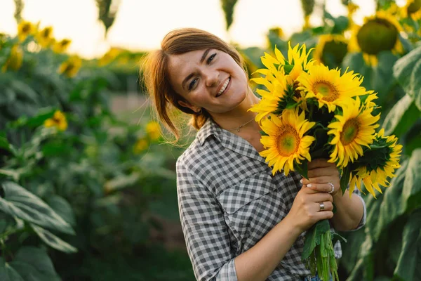 Schöne junge Frau mit Sonnenblumen genießt die Natur und lacht auf sommerlichem Sonnenblumenfeld. — Stockfoto