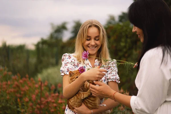 Eine junge Mutter mit einer Tochter im Teenageralter spielt mit einer Ingwerkatze im Garten. — Stockfoto